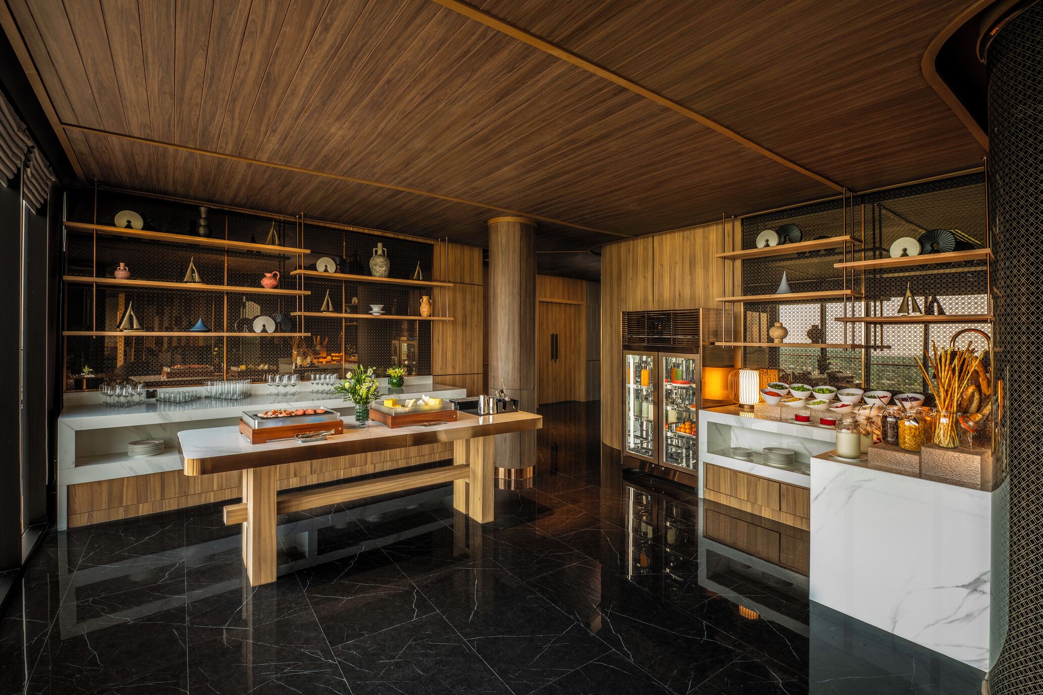 A modern kitchen with wooden cabinetry, marble countertops, and open shelving displaying kitchenware.