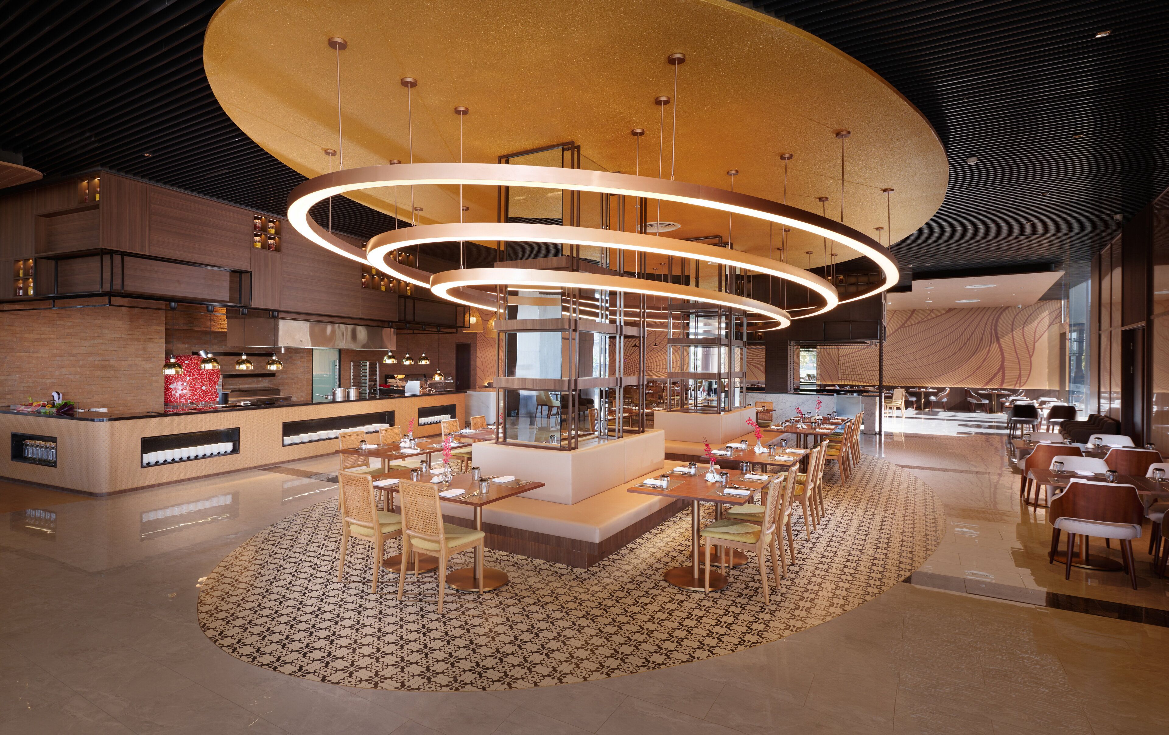 Um restaurante moderno com área de estar central, cozinha ao fundo e um grande lustre circular.