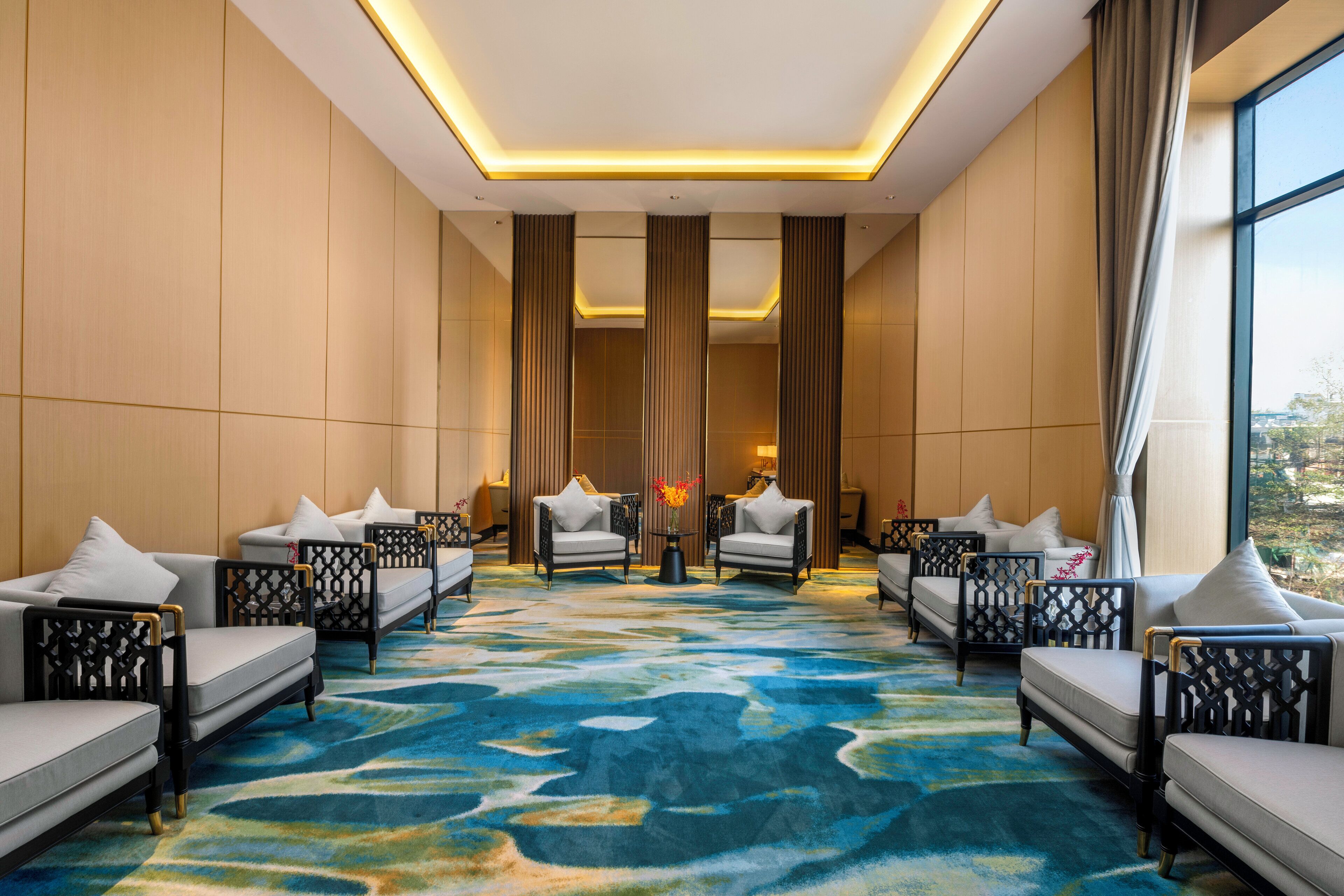 A hotel lobby with a central seating area, large windows, and a patterned carpet.