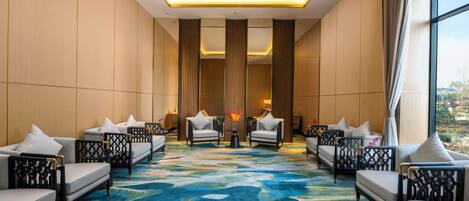 A hotel lobby with a central seating area, large windows, and a patterned carpet.