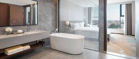 A modern bathroom with a large mirror, a bathtub, and a view of a cityscape through a glass door.
