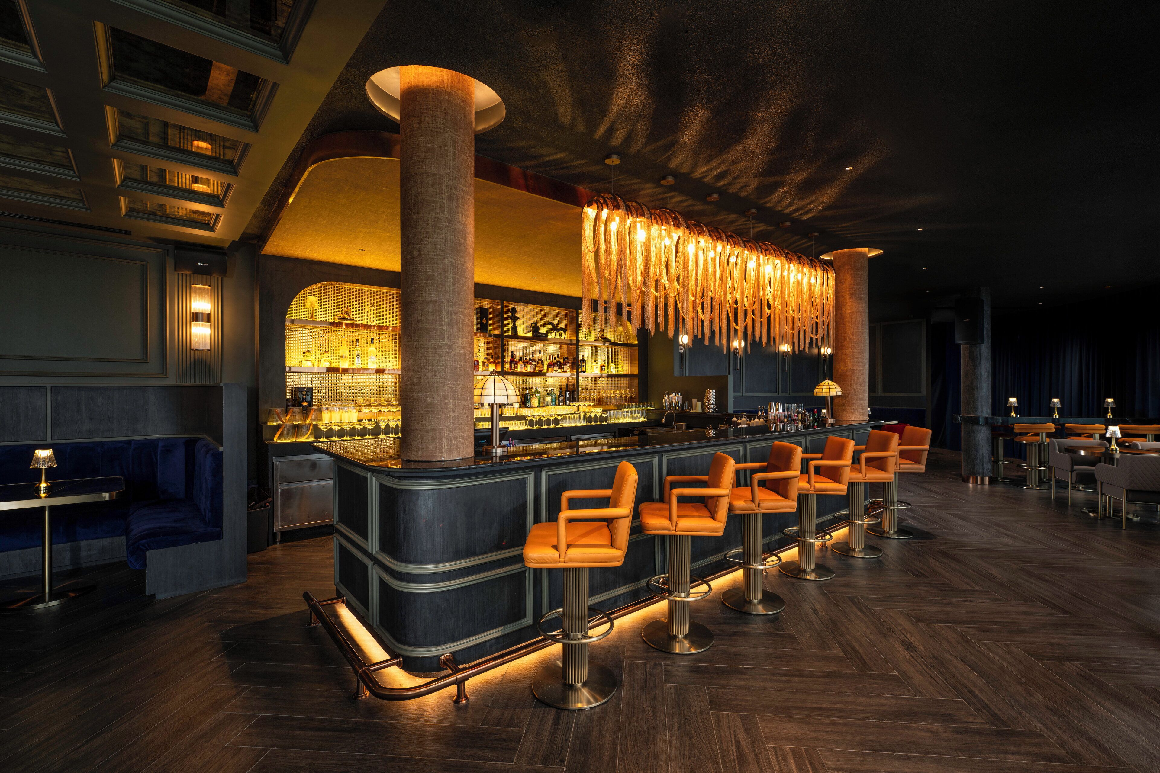 A bar area with a long counter, multiple bar stools, and a bar stocked with bottles.