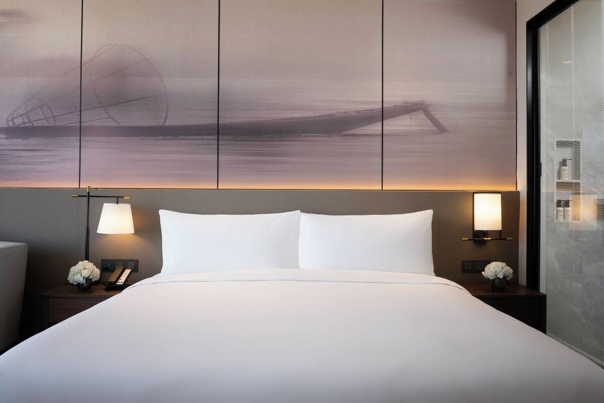 A hotel room with a large bed, two bedside lamps, and a wall-mounted artwork depicting a boat.