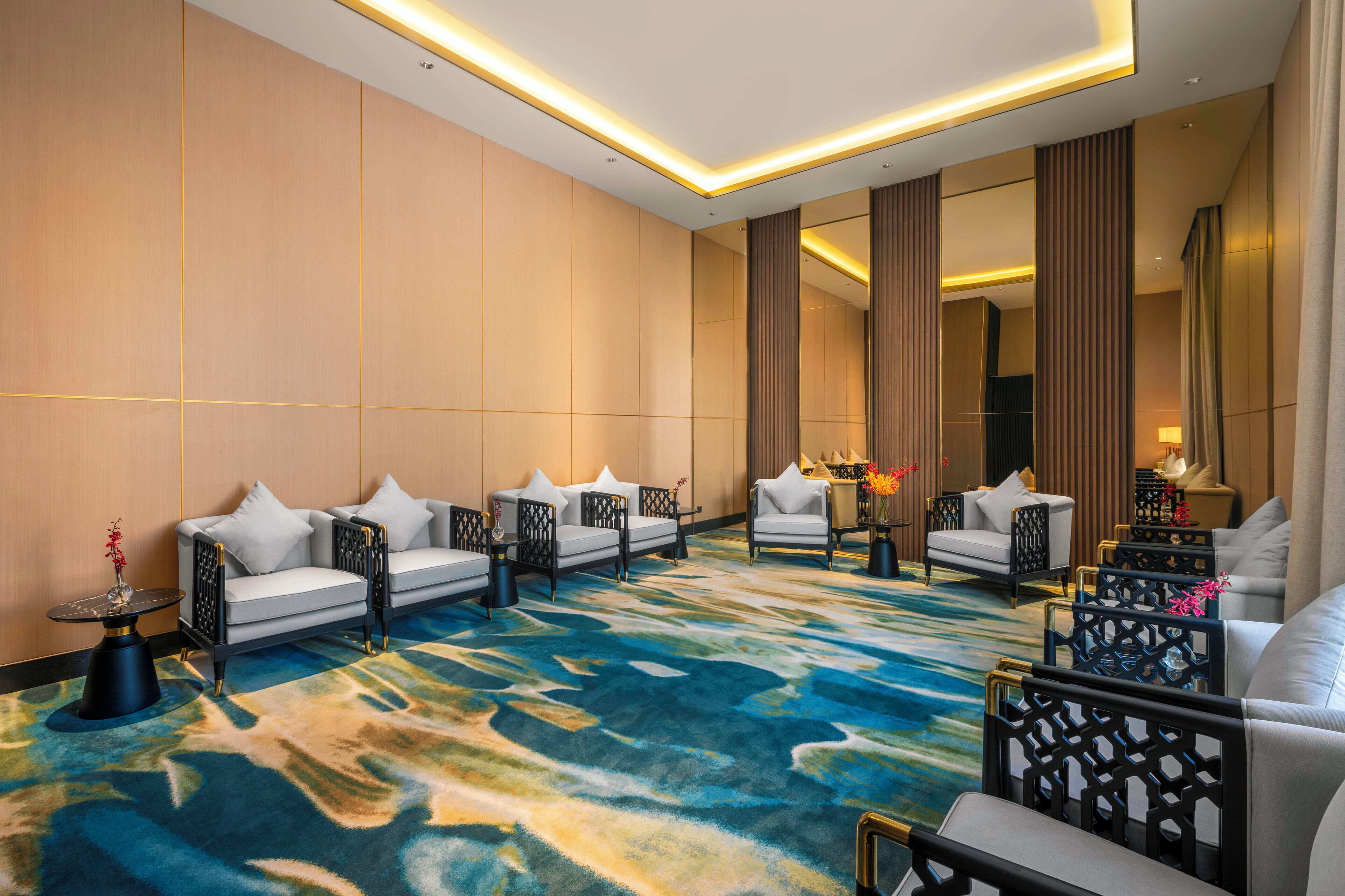 A hotel lobby with a blue and green patterned carpet, white sofas, and black-framed chairs.