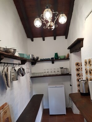 Uma cozinha compacta com geladeira branca, um banco de madeira e luminária pendente.
