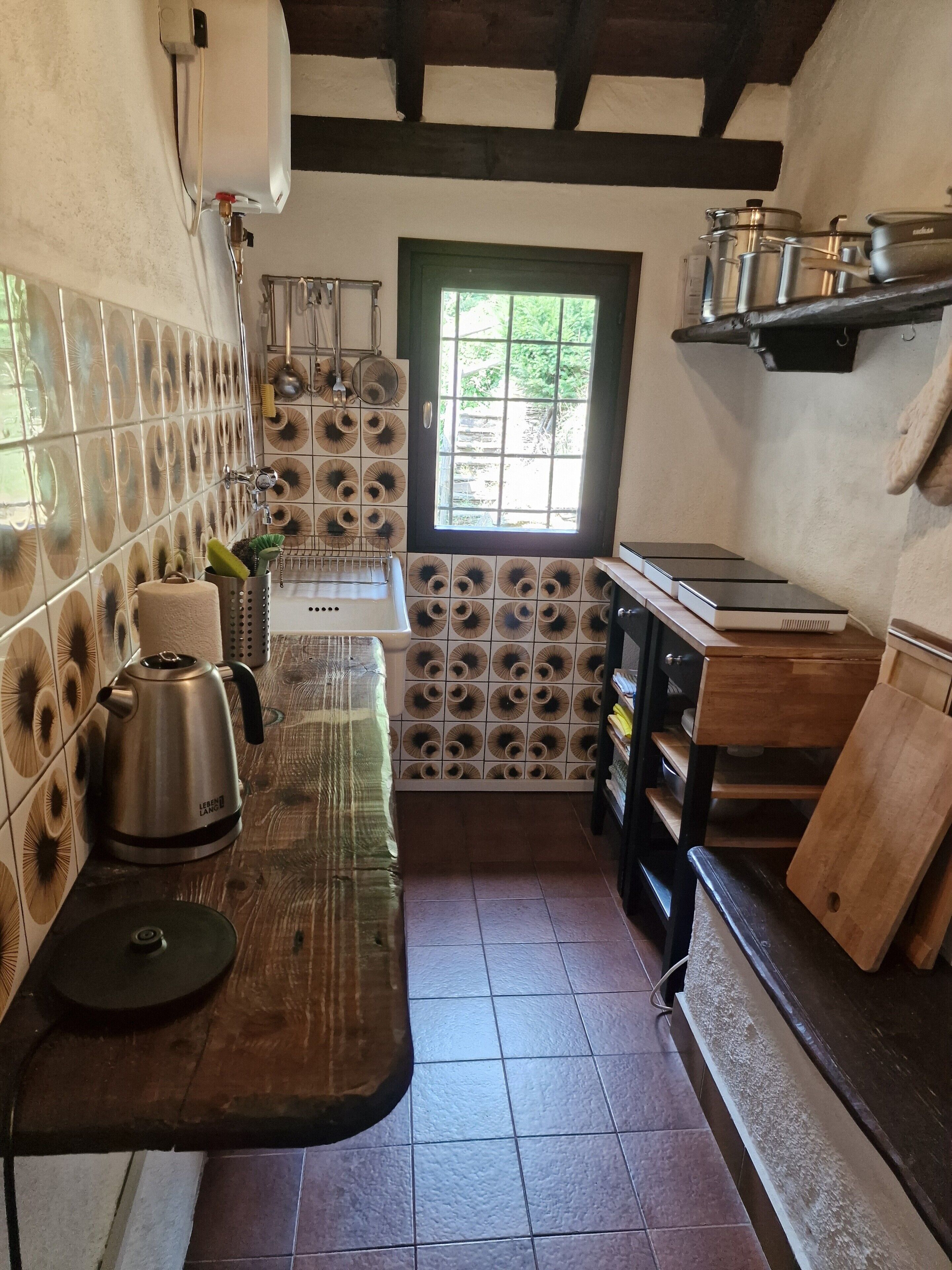 Una cocina con encimera de madera, una tetera y una ventana con vistas a follaje.