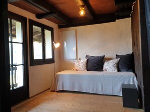 A bedroom with a bed, a window, a wall-mounted light, and a wooden floor.