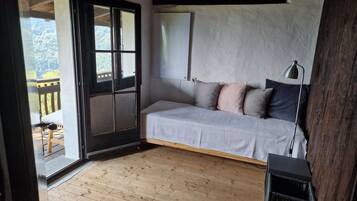 Une pièce avec un plancher en bois, un lit avec des oreillers, un bureau avec une lampe et une fenêtre donnant sur des arbres.