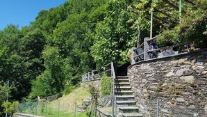 A stone staircase leading up a hill with a metal railing, surrounded by greenery and a clear sky.