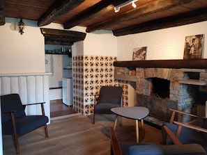 Um interior acolhedor com lareira de pedra, vigas de madeira e um espaço de estar com cadeiras e uma mesa pequena.
