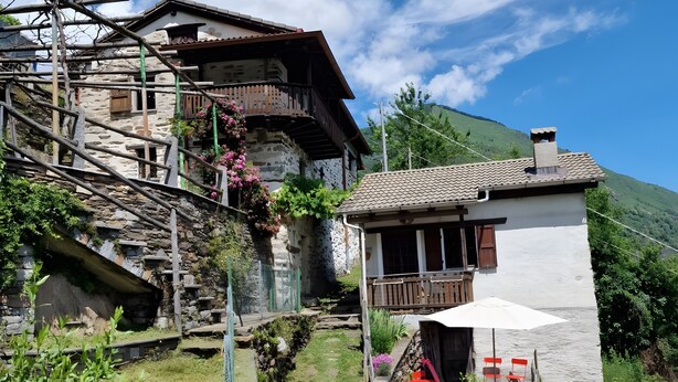 A traditional stone house with a wooden balcony, a stone pathway, and a view of a mountain.