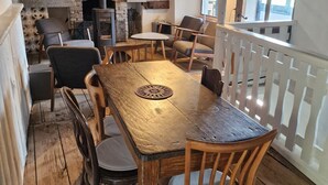A rustic interior with a wooden dining table, chairs, a fireplace, and a white railing.
