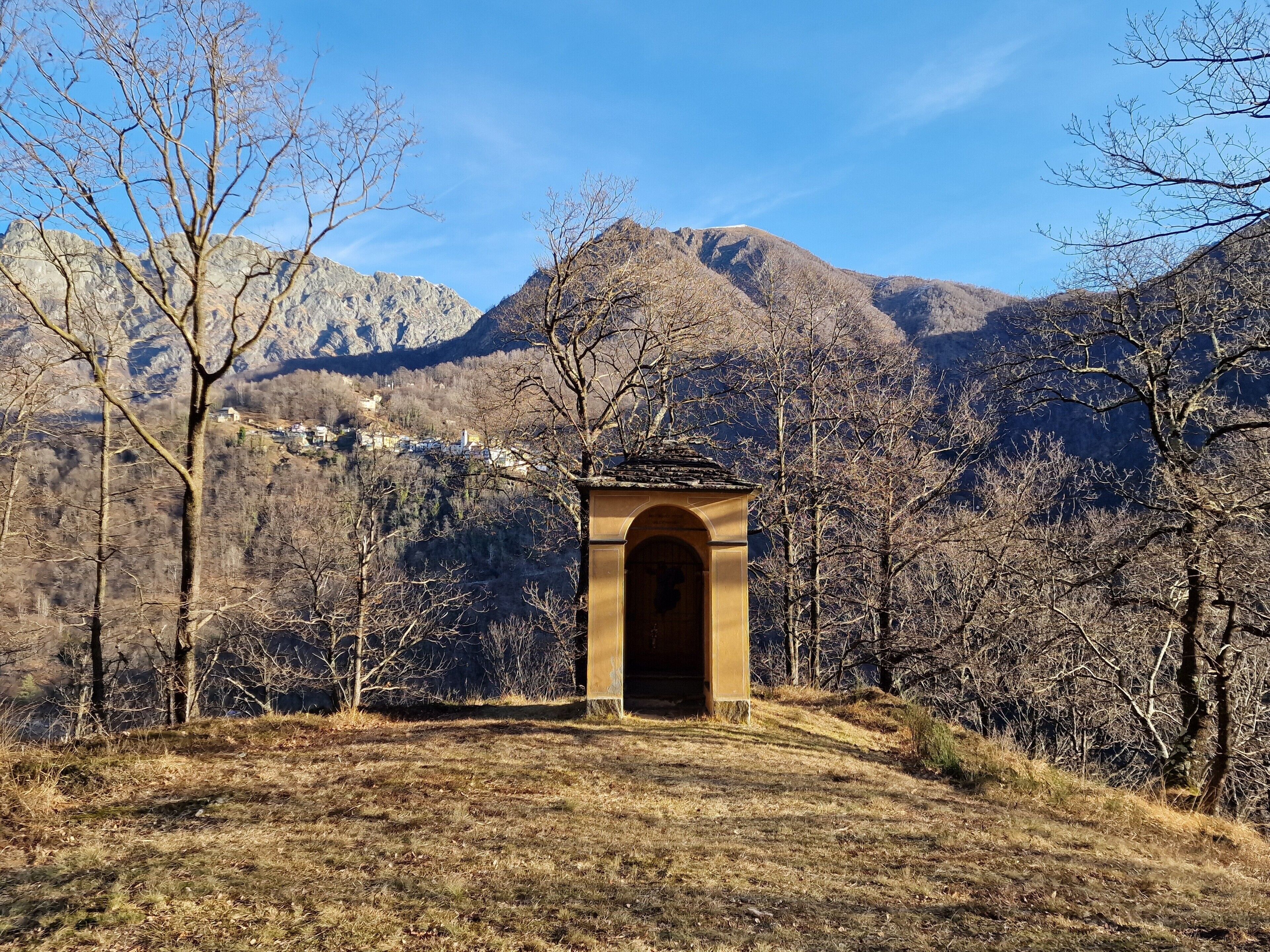 A mountainous landscape with a stone archway leading to a building, surrounded by bare trees.