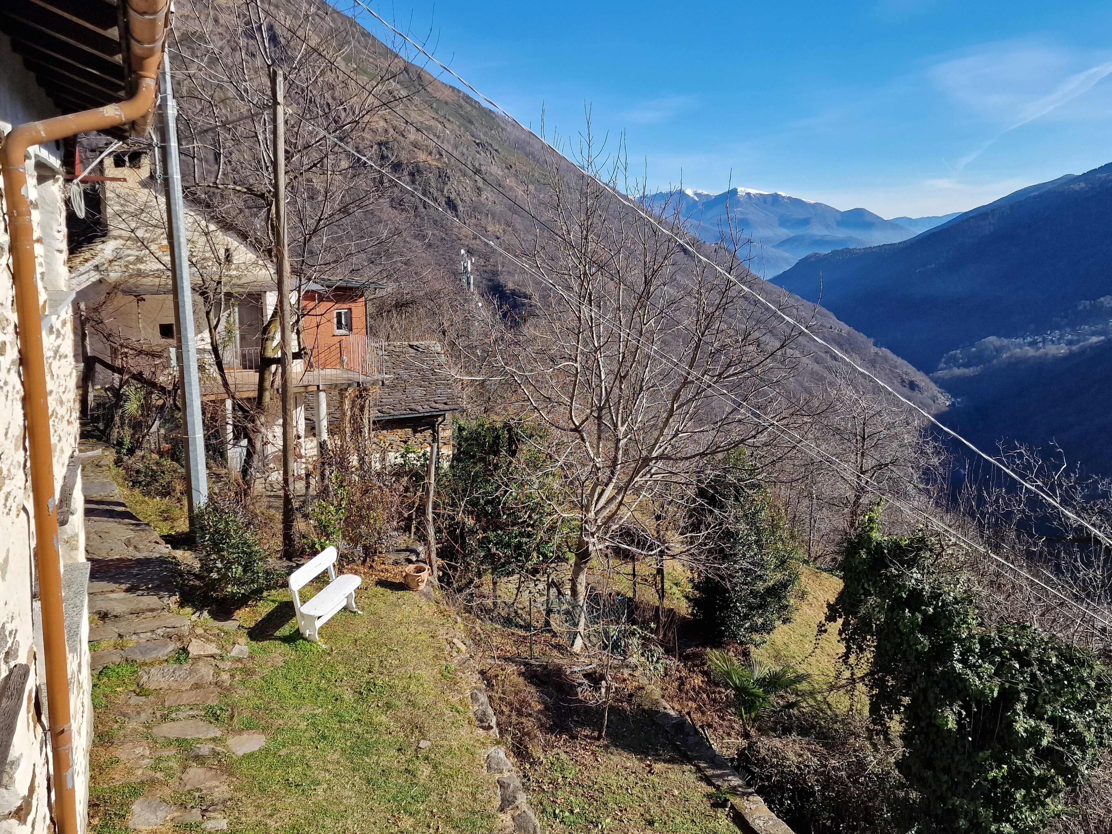 Paesaggio montuoso con un sentiero di pietra che conduce a un edificio rustico con un balcone.