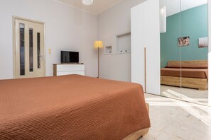 Een slaapkamer met een bed, een televisie, een lamp, een kledingkast en een schuifdeur naar een andere kamer.