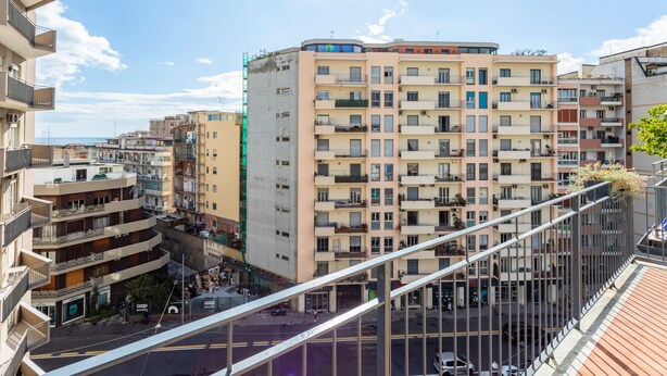 A multi-story building with balconies, a street below, and a clear sky.