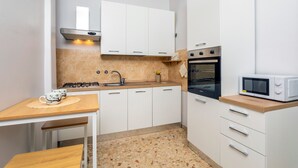 A compact kitchen with white cabinets, a built-in oven, a microwave, and a small table with a cup.