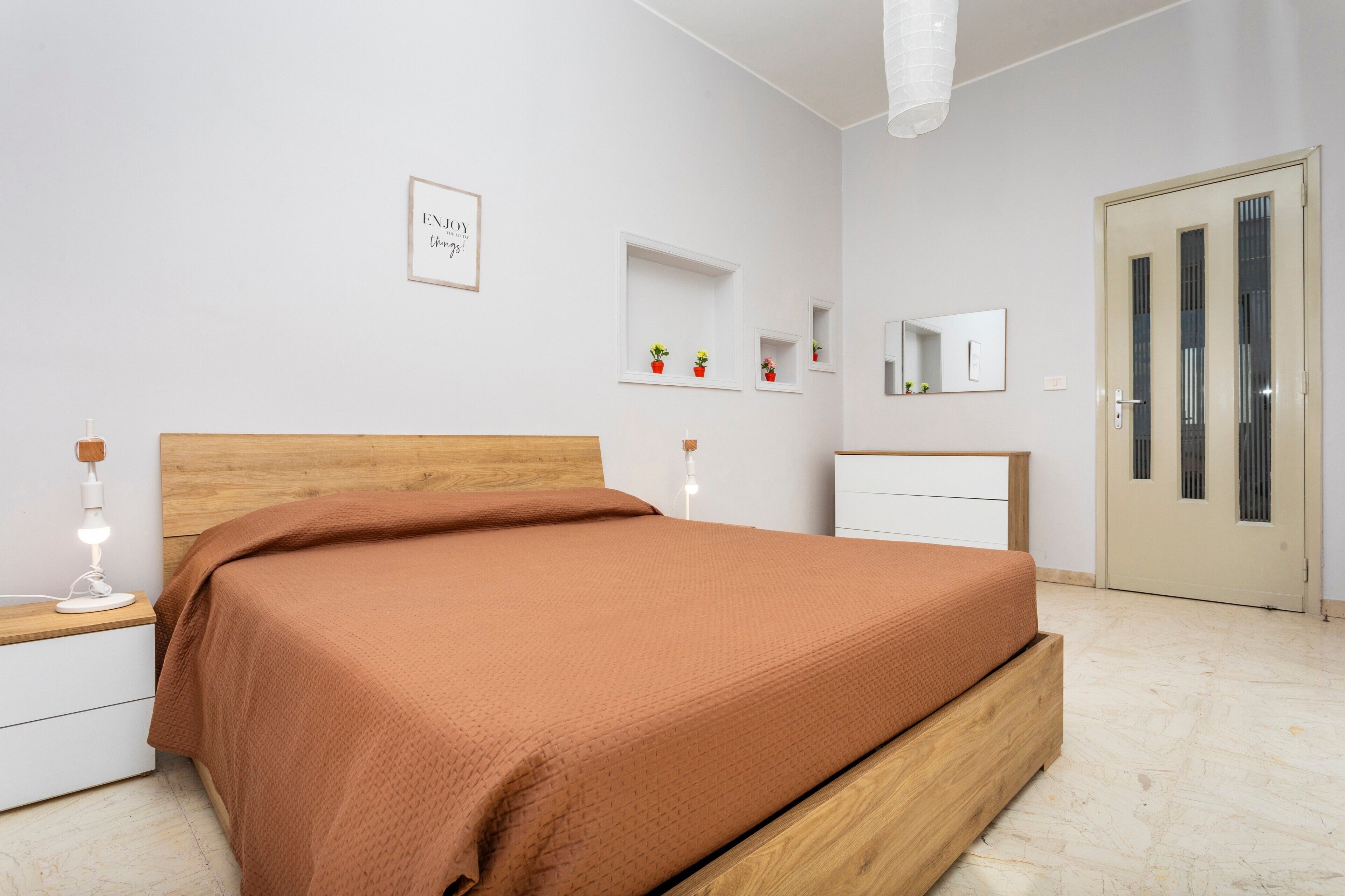 A bedroom with a wooden bed, bedside table, nightstand, and a door with a mirror.