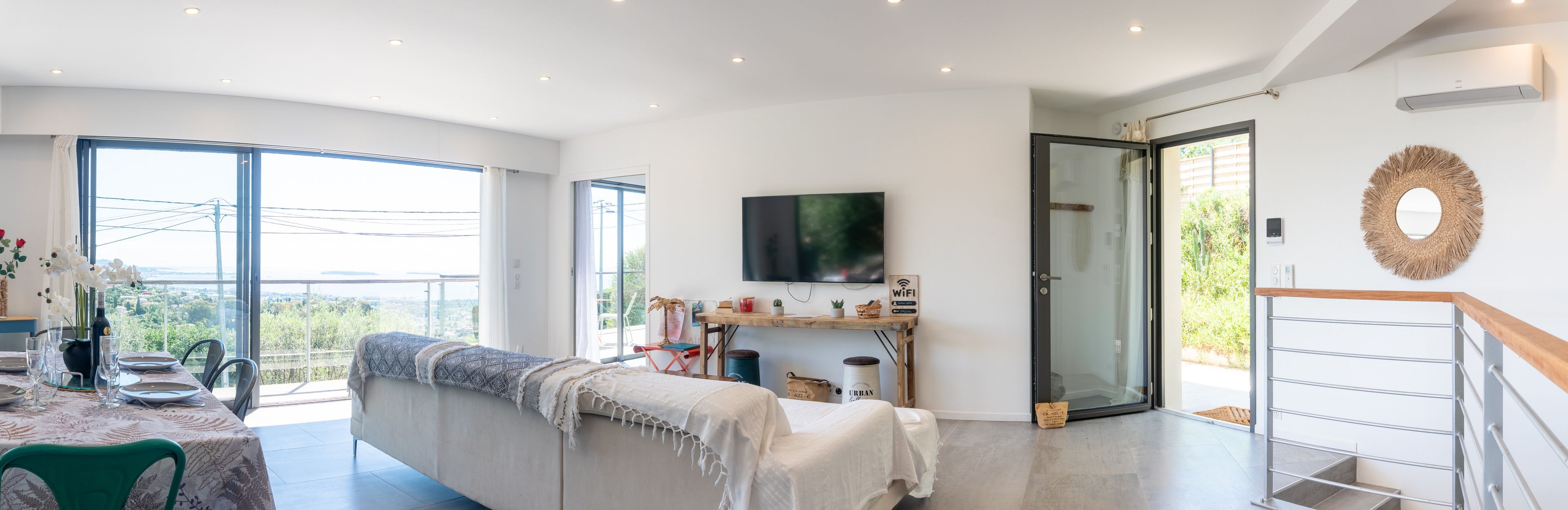 En moderne stue med sofa, spisebord og fjernsyn ophængt på væggen.
