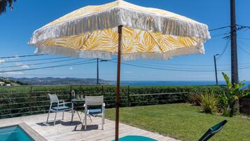 Et poolområde med træterrasse, et bord med stole og en stor parasol.