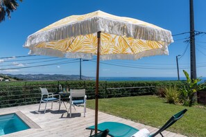 Een zwembadgedeelte met een houten terras, een tafel met stoelen en een grote parasol.