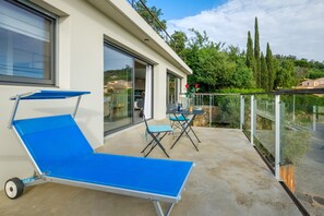 A modern outdoor balcony with a blue sun lounger, two chairs, and a table. - Contemporary villa with panoramic views over Cannes Bay and private pool (Mandelieu-la-Napoule)