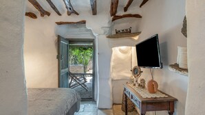 Ein schmales Zimmer mit einem Bett, einem Fernseher und einem kleinen Tisch mit einem Teekessel.