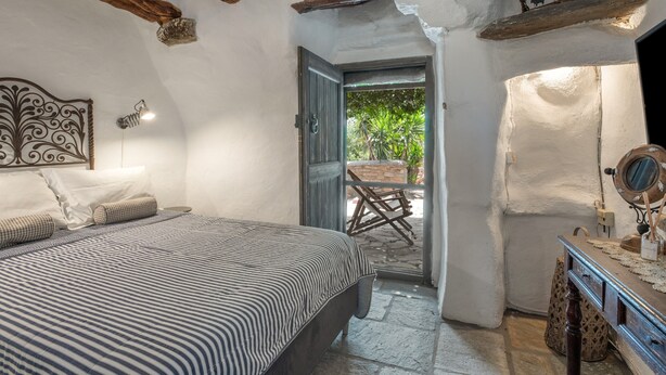 Ein Schlafzimmer mit einem Bett, einem Holz-Kopfteil, einem kleinen Tisch mit Spiegel und einer Tür zu einem Außenbereich.