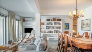 A living room with a sofa, dining table, chairs, a bookshelf, and a television. - Apartment In A Hotel 'Anemos Suite with Private Pool' with Sea View, Wi-Fi and Air Conditioning (Laouti Tinos)
