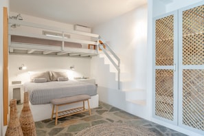 A bedroom with a bunk bed, a bedside table, a bench, and a staircase with a wooden railing.
