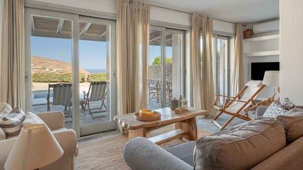 A living room with a sofa, chairs, a table, and a view through large glass doors to an outdoor patio. - Apartment In A Hotel 'Anemos Suite with Private Pool' with Sea View, Wi-Fi and Air Conditioning (Laouti Tinos)