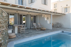 A poolside area with a table and chairs, a bicycle, and a stone wall.