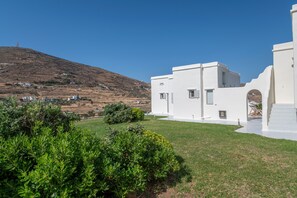 Un bâtiment blanc avec un toit plat, une petite fenêtre et une porte. Il y a un espace herbeux devant le bâtiment.