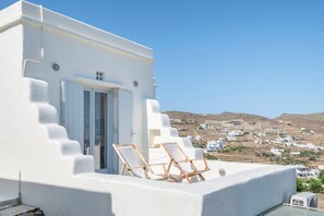 Un edificio blanco con un balcón, una puerta y dos sillas de madera.