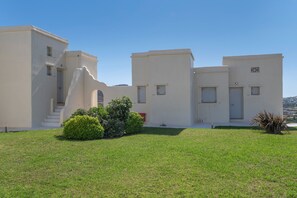 A modern building with a flat roof, a staircase leading to the entrance, and a well-maintained lawn. - Apartment In A Hotel 'Anemos Standar Double Room 4' with Sea View, Wi-Fi and Air Conditioning (Laouti Tinos)