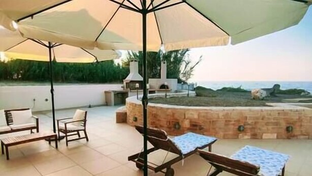 An outdoor patio with a brick fire pit, lounge chairs, and umbrellas. - Aqua Luna Bay Beachfront Luxury Apartment (Pigianos Kampos)