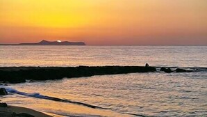 A sunset over a calm sea with a rocky shoreline. - Aqua Luna Bay Beachfront Luxury Apartment (Pigianos Kampos)