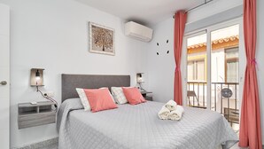 Une chambre d’hôtel comprenant un lit, des tables de chevet, un climatiseur fixé au mur, une fenêtre avec des rideaux et un balcon avec une chaise.
