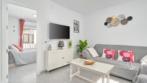 Un salon moderne avec un téléviseur à écran plat, un canapé, une table basse et un lit agrémenté d’un rideau rose.