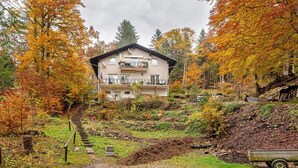 Un bâtiment à deux étages doté d’un balcon, entouré d’un feuillage automnal.