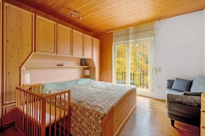 A bedroom with a wooden bed, a crib, a sofa, and a large window with a view of trees. - Holiday Apartment 'Ferien Bei Waltraud Weiss' with Mountain View, Shared Terrace and Wi-Fi (Ruffré Mendola TN)