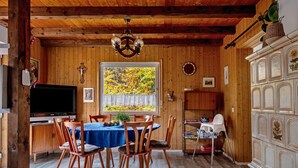 Une pièce aux murs lambrissés, comprenant une table à manger, des chaises, un téléviseur et une fenêtre donnant sur des arbres.