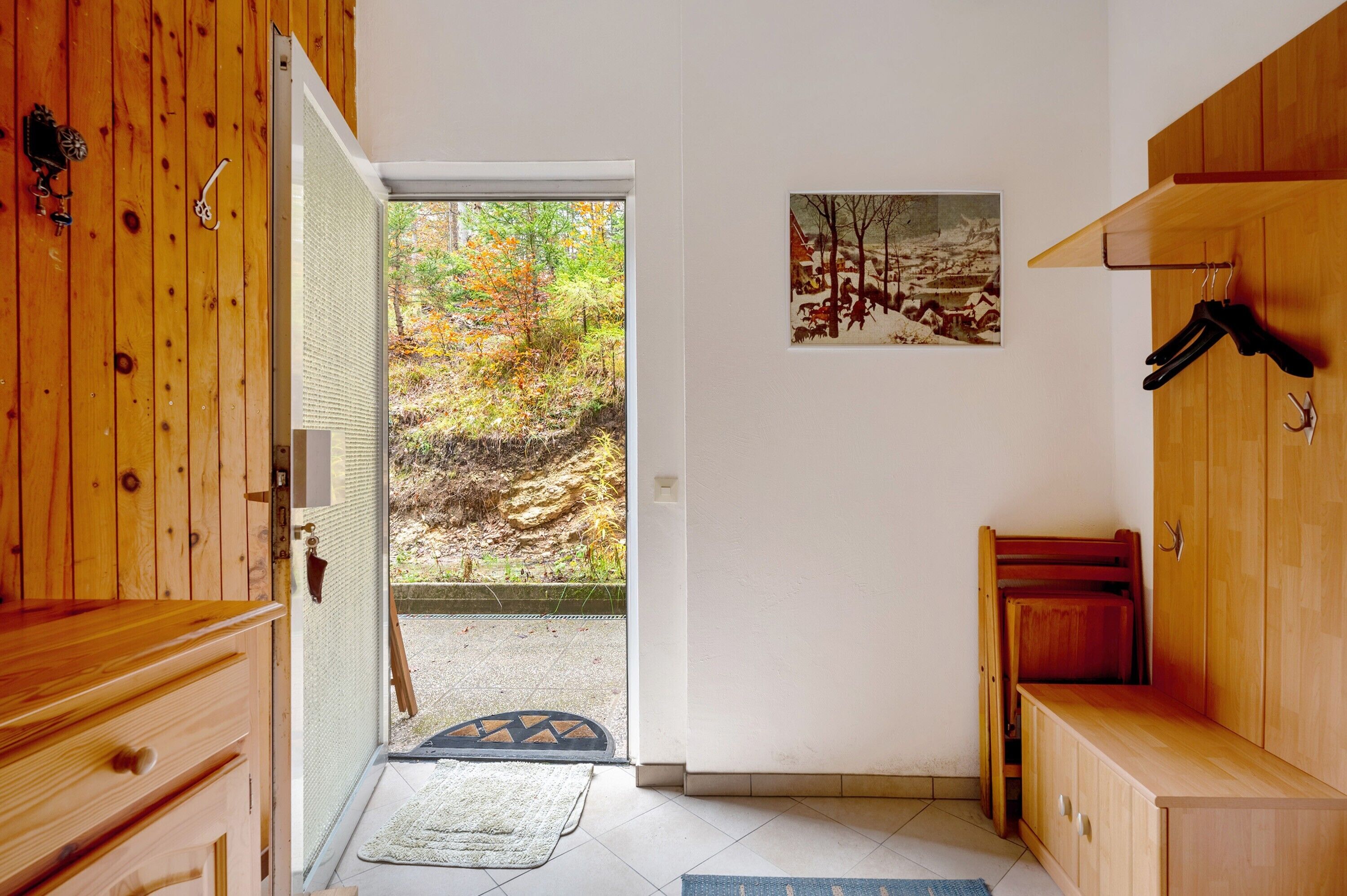 Un intérieur en bois avec une porte donnant sur un espace extérieur, un tableau accroché au mur et un banc.