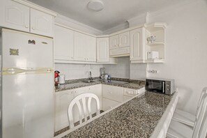 A compact kitchen with white cabinets, a granite countertop, a white chair, a toaster, and a microwave. - Vacation 'Ceyla' with Sea View, Private Terrace and Wi-Fi (Arona)