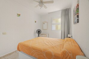 A bedroom with a bed, a ceiling fan, a window with curtains, a bedside table, and a wall-mounted mirror. - Vacation 'Ceyla' with Sea View, Private Terrace and Wi-Fi (Arona)