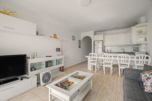 A modern living room with a flat-screen TV, a coffee table, and a dining area with white chairs and a kitchen with white cabinets. - Vacation 'Ceyla' with Sea View, Private Terrace and Wi-Fi (Arona)