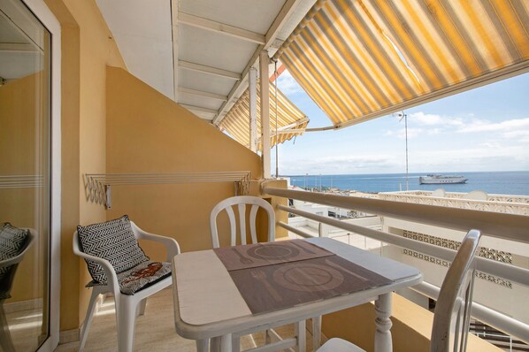 A balcony with a table and chairs, a striped awning, and a view of the sea and a boat. - Vacation 'Ceyla' with Sea View, Private Terrace and Wi-Fi (Arona)