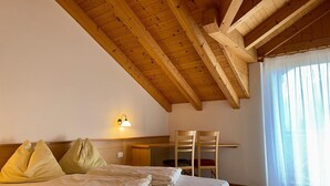 A bedroom with a wooden ceiling, a bed with pillows, a desk, and a chair.