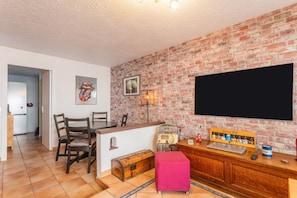 A kitchen with a brick wall, a flat-screen TV, a jukebox, and a red ottoman.