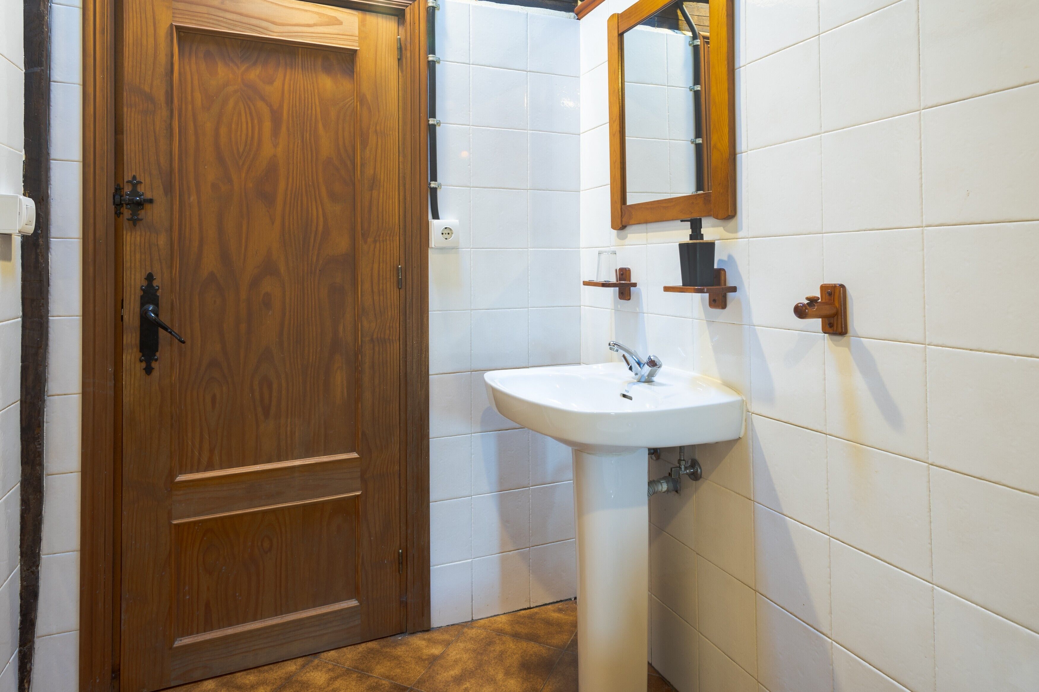 A wooden door with a handle, a white sink with a mirror above it, and a tiled wall.